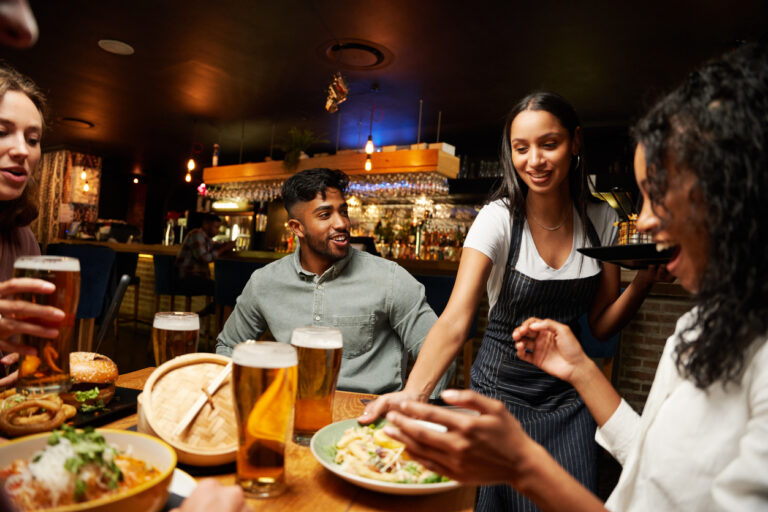 Young multiracial group of friends wearing casual clothing smiling while receiving dinner from waitress